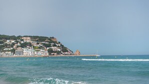 A coastal town with buildings on a hillside, a rocky outcrop, and the sea with buoys.