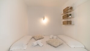 A minimalist bedroom with a bed, pillows, a wall-mounted shelf with baskets, and a wall-mounted light.