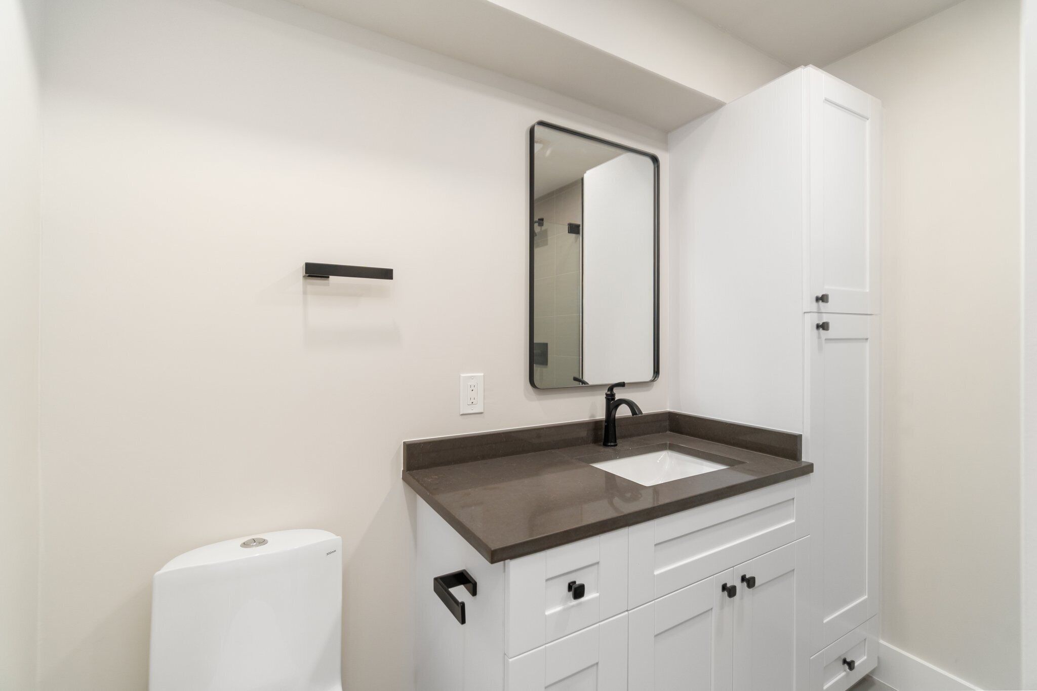 Une salle de bain moderne avec un meuble-lavabo blanc, un robinet noir, un grand miroir et des toilettes blanches.