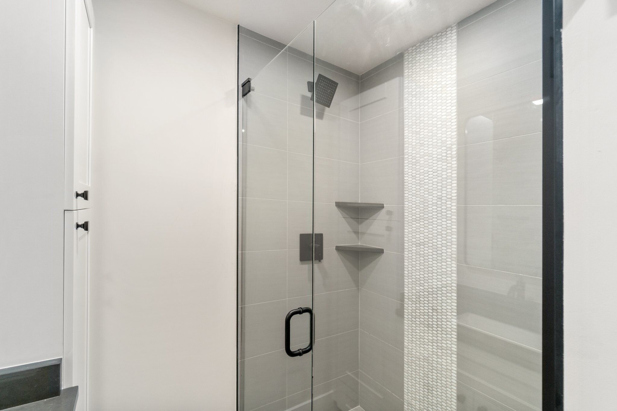 Een moderne douche met een glazen deur, een zwarte hendel en een gestructureerde wand.
