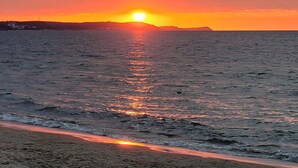Un coucher de soleil sur une mer calme, avec une plage au premier plan.