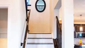 Eine Holztreppe mit schwarzer Geländer, die zu einem Küchenbereich mit modernen Geräten und einem Barhocker führt.