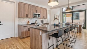 A modern kitchen with wooden cabinets, a central island with bar stools, stainless steel appliances, and pendant lighting. - 120 Cedar Dr | Slopeside, Hot Tub, Mtn Views (Winter Park)