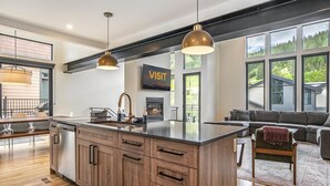 A modern kitchen with wooden cabinets, a central island, pendant lighting, and a dining area with a view of the outdoors. - 120 Cedar Dr | Slopeside, Hot Tub, Mtn Views (Winter Park)