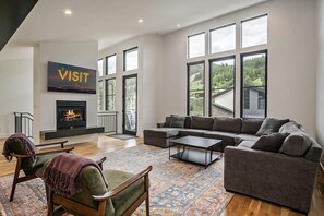 A spacious living room with a fireplace, large windows, a sectional sofa, and a cozy fireplace area.