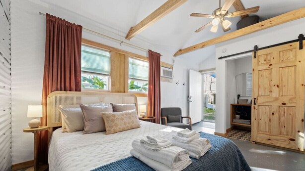 Un dormitorio con una cama grande, vigas de madera, un ventilador de techo y vistas al exterior.