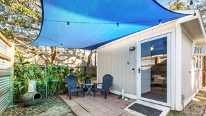 Un pequeño espacio exterior con mesa y sillas de patio, una vela azul y una puerta que da a una habitación interior.