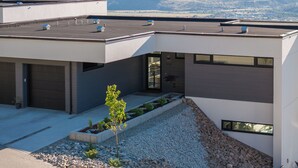 A modern building with a flat roof, large windows, and a view of mountains in the background.