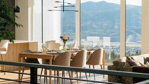 A modern dining area with a large table, chairs, and a view of mountains through large windows.