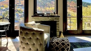 A living room with a fireplace, a comfortable armchair, and a view of a mountainous landscape through large windows. - Dual-Unit Mountain Retreat: 4BR,  Prime Location, Sleeps 10, Historic Charm & Modern Luxury, Steps to Main St! (Park City)