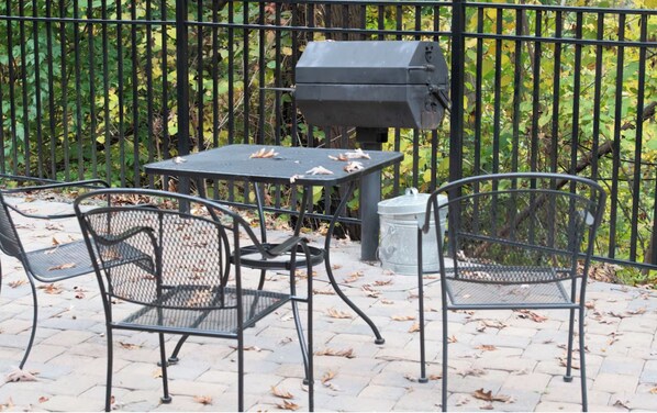 Un patio exterior con una parrilla, dos sillas de metal y una mesa.
