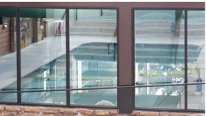 Vista a través de una ventana con base de piedra, que refleja un edificio con escaleras y un área cubierta.