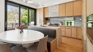Una cocina moderna con armarios de madera, encimera de mármol y zona de comedor con mesa y sillas redondas.