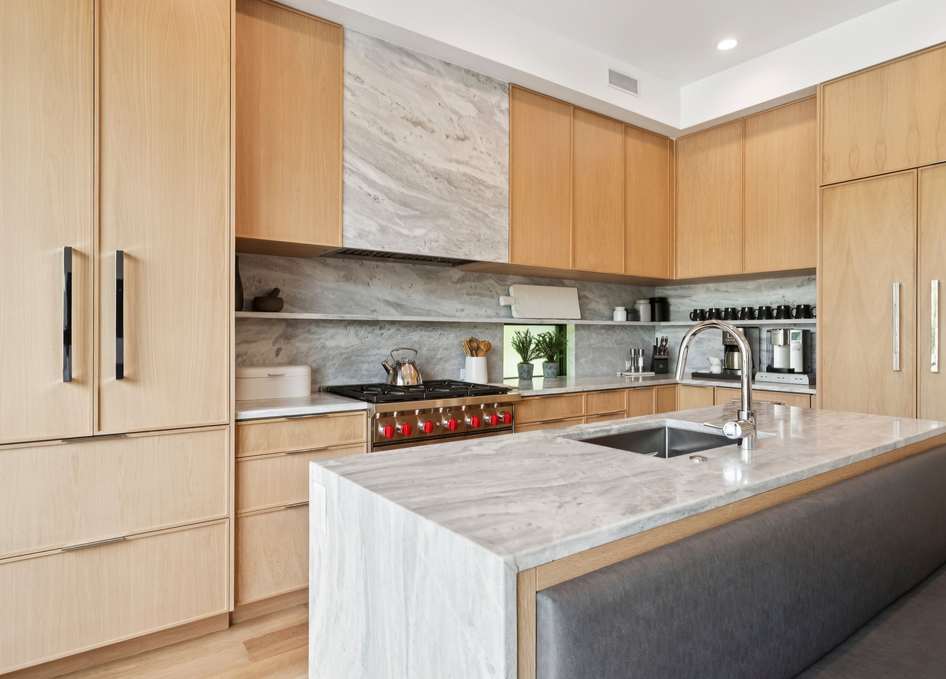 Una cocina moderna con armarios de madera, salpicadero de mármol, estufa de acero inoxidable y un lavamanos con grifo.