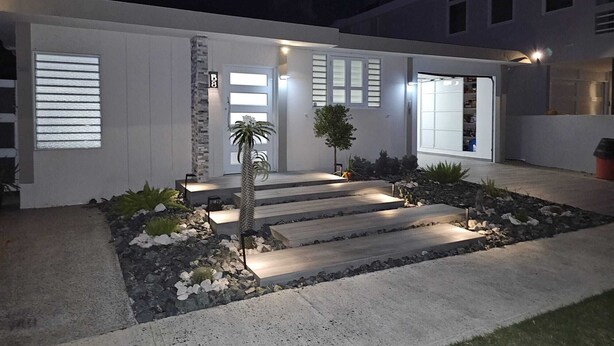 Una casa moderna con una entrada bien iluminada, un pequeño jardín y un garaje.