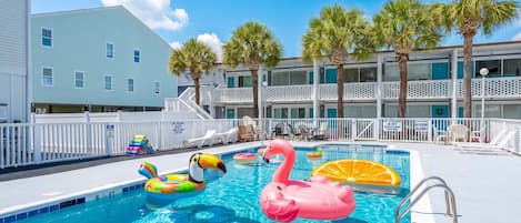 A swimming pool with inflatable toys, a lifeguard stand, and a building with balconies.
