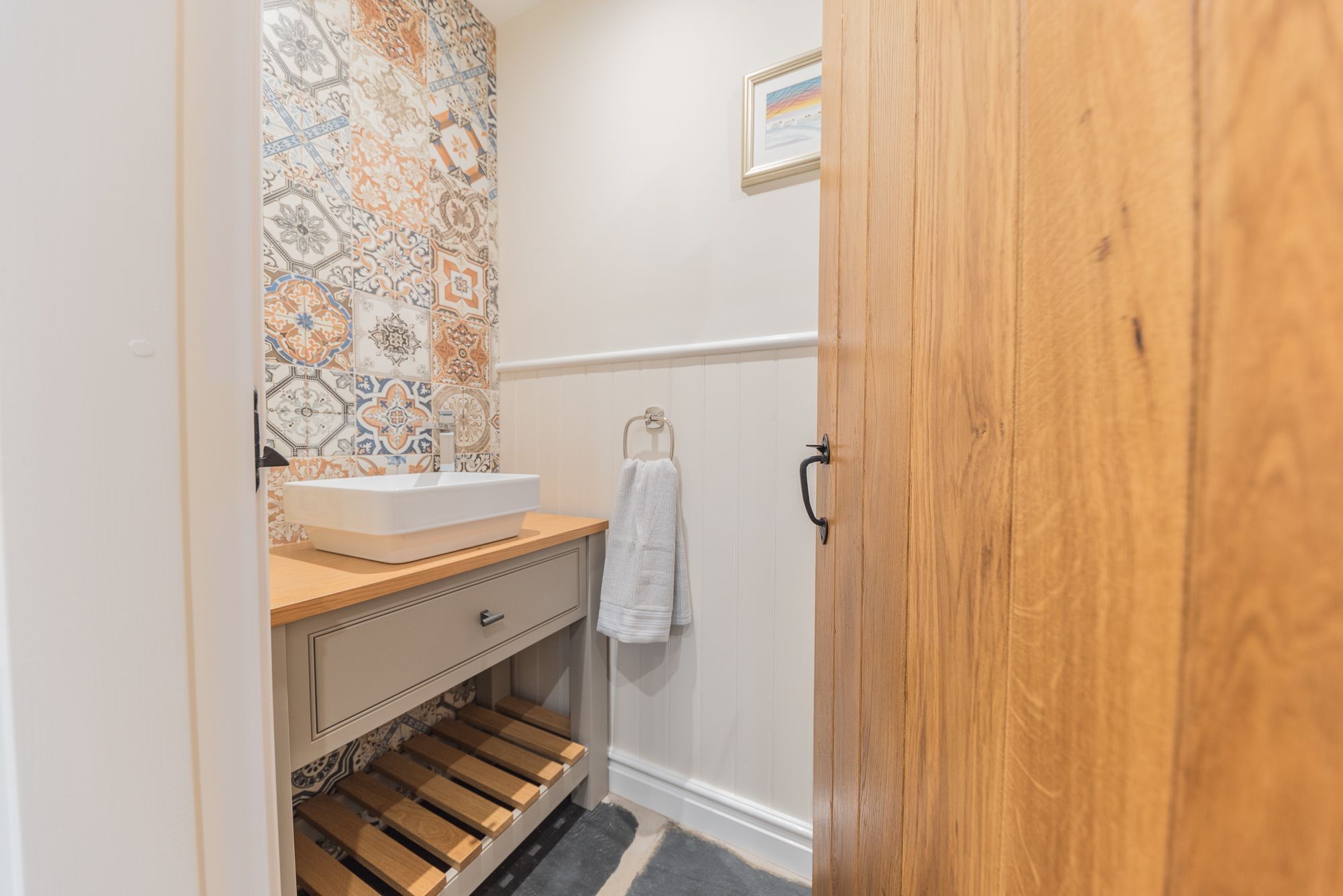Une salle de bain avec un mur recouvert de carreaux derrière le lavabo, un lavabo, un porte-serviettes et une porte en bois.