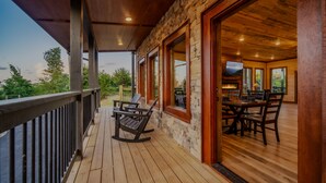 A wooden deck with a stone wall, a dining area with a table and chairs, and a view of the outdoors.