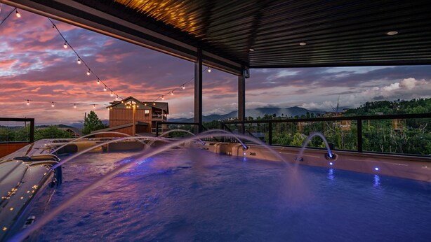 Un bain à remous doté de plusieurs jets, une terrasse en bois et une vue sur une chaîne de montagnes au coucher du soleil.
