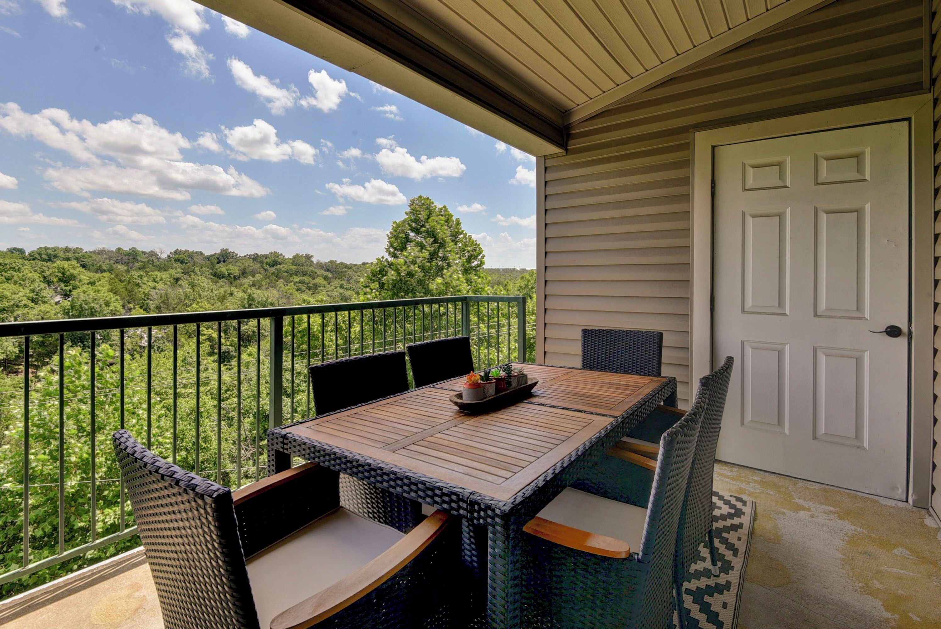 A balcony with a table and chairs, overlooking a lush green landscape.