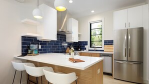 Una cocina moderna con una isla central, taburetes de bar, un refrigerador de acero inoxidable y una ventana que proporciona luz natural.