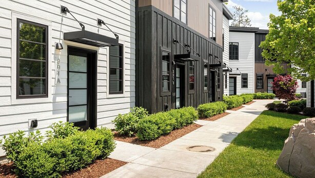 A row of modern townhouses with a clean, minimalist design, featuring large windows and a well-maintained front yard with shrubs and a pathway.
