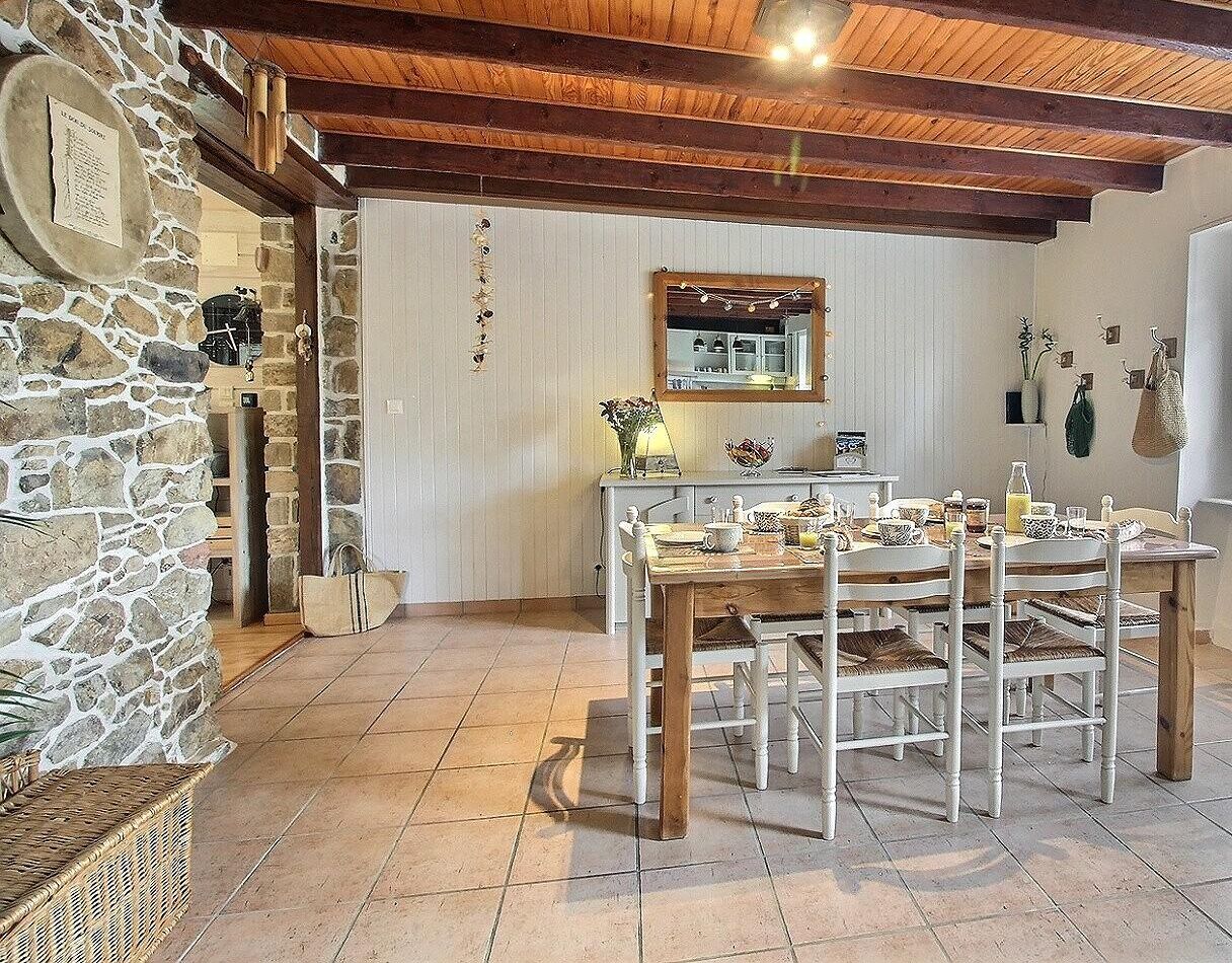 A rustic dining area with a stone wall, wooden ceiling beams, and a tiled floor.
