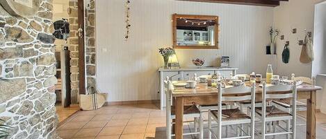A rustic dining area with a stone wall, wooden ceiling beams, and a tiled floor.