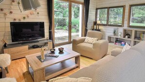 Una sala de estar acogedora con un televisor de pantalla plana, un sofá color beige, una mesa de centro de madera y un ventanal con vistas al exterior.