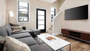 Een moderne woonkamer met een hoekbank, een salontafel, een flatscreen-tv en een trap.