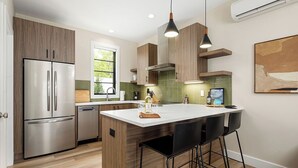 Een moderne keuken met houten kastjes, een roestvrijstalen koelkast, een wit kookeiland met barkrukken en hanglampen.