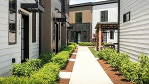 A modern building with a central pathway flanked by neatly trimmed bushes and a small garden area with flowers.