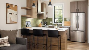 A modern kitchen with wooden cabinets, a stainless steel refrigerator, and a bar area with stools.