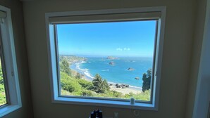 A room with a large window overlooking a coastal landscape, a small table with binoculars, and blue upholstered chairs.