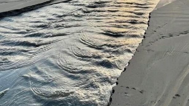 A beach with waves, rocks, and a sunset.
