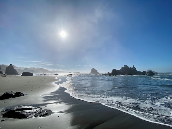 A beach with large rocks, clear skies, and sunlight reflecting on the water.