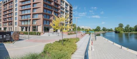 A modern building with multiple floors, a paved walkway, and a river in the background.
