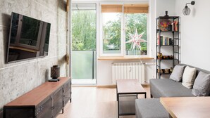 Un salon moderne avec un téléviseur fixé au mur, un banc en bois, un canapé gris et une bibliothèque remplie de livres et d’objets décoratifs.