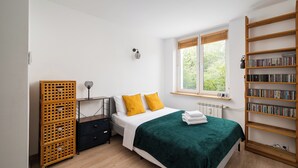 Une chambre à coucher comprenant un lit, une table de chevet, une bibliothèque en bois et une fenêtre avec des stores.