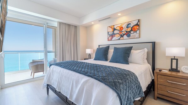 A modern hotel room with a large bed, a nightstand, a lamp, and a painting on the wall.