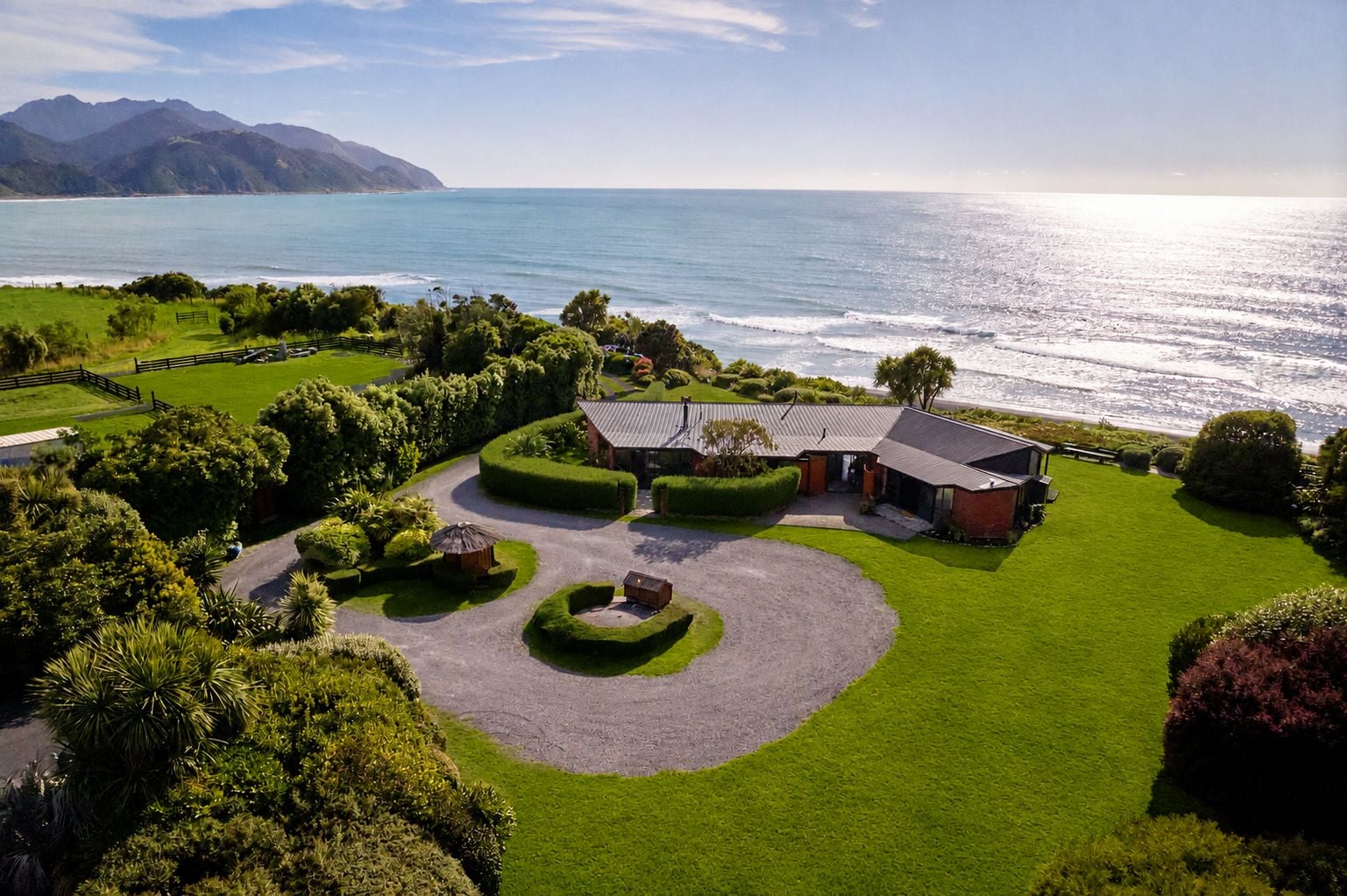 A coastal property with a well-maintained lawn, a circular driveway, and a building with a sloped roof.