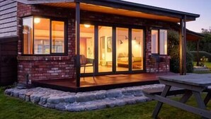 Ett hus med en inglasad veranda, stora glasdörrar och en stensatt gång som leder till ett picknickbord.