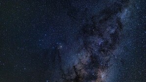 Céu noturno estrelado com um aglomerado denso de estrelas e uma galáxia visível.