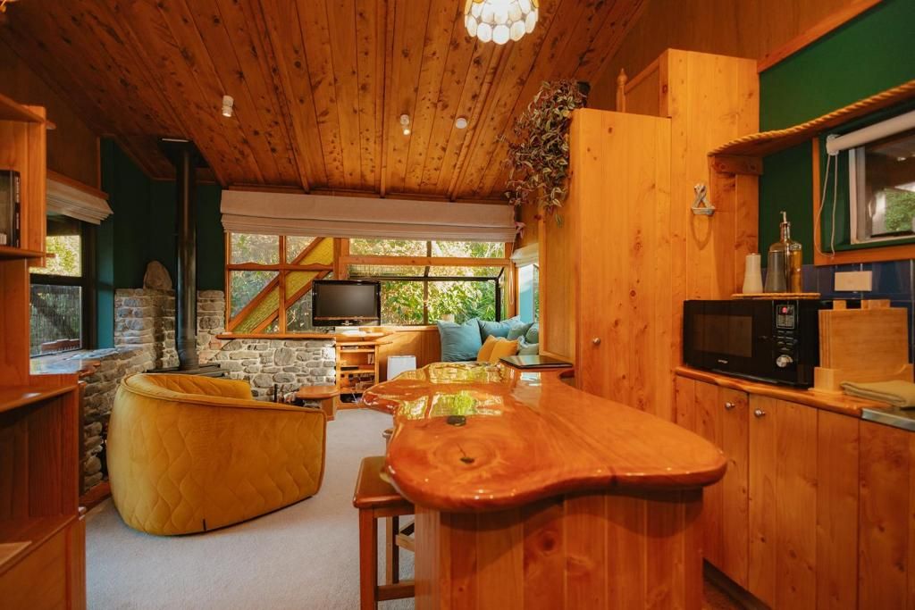 A cozy cabin interior with a wooden ceiling, a stone fireplace, a television, and a kitchen area with a microwave.