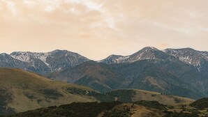 Paisagem montanhosa com picos nevados e colinas ondulantes.