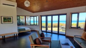 Een ruime kamer met een groot raam met uitzicht op de oceaan, een bed en zithoeken.