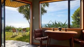 Een kamer met een tafel en stoelen, grote ramen met uitzicht op groen en een verafgelegen landschap.