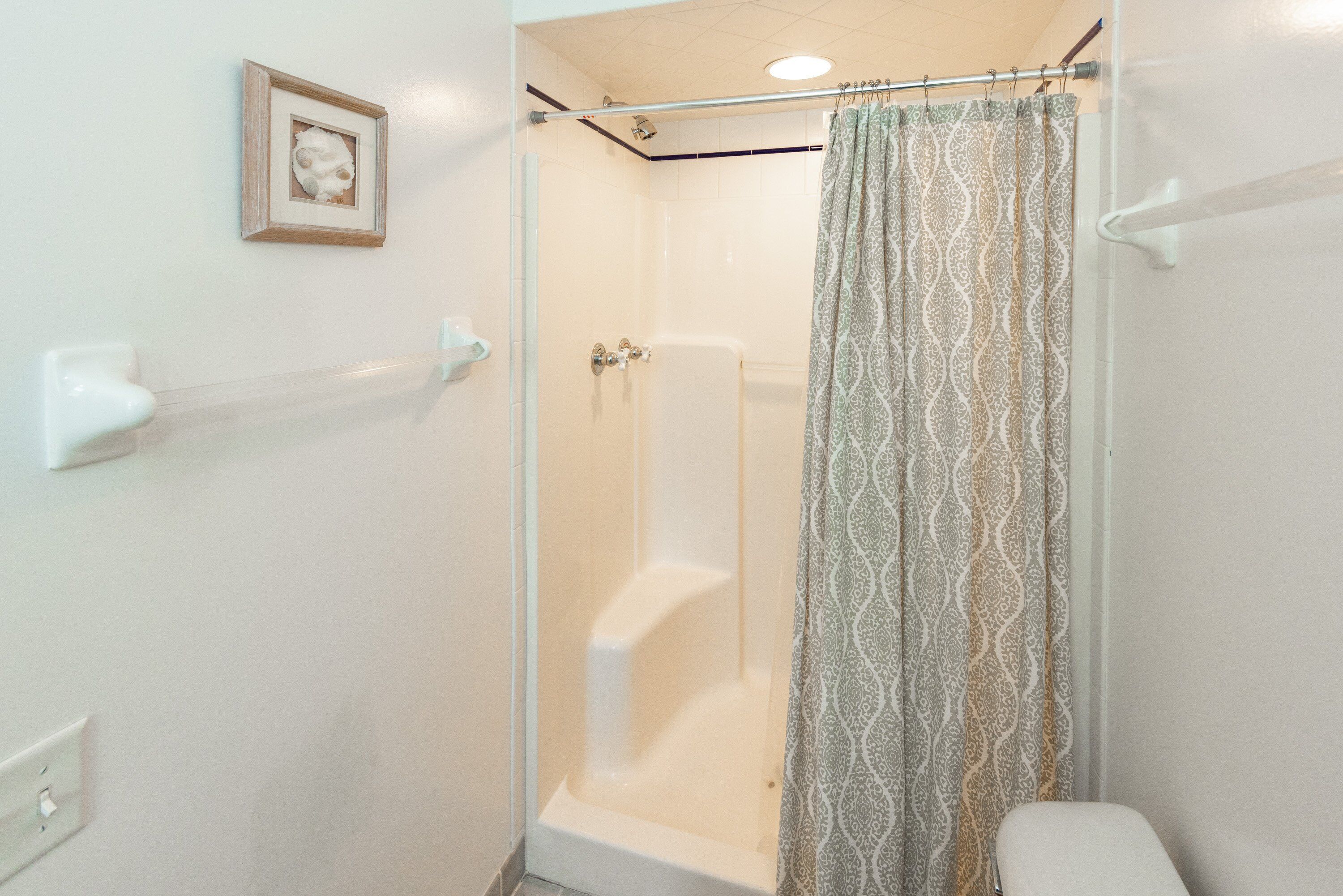 A shower with a glass door, a towel rack, and a patterned shower curtain.