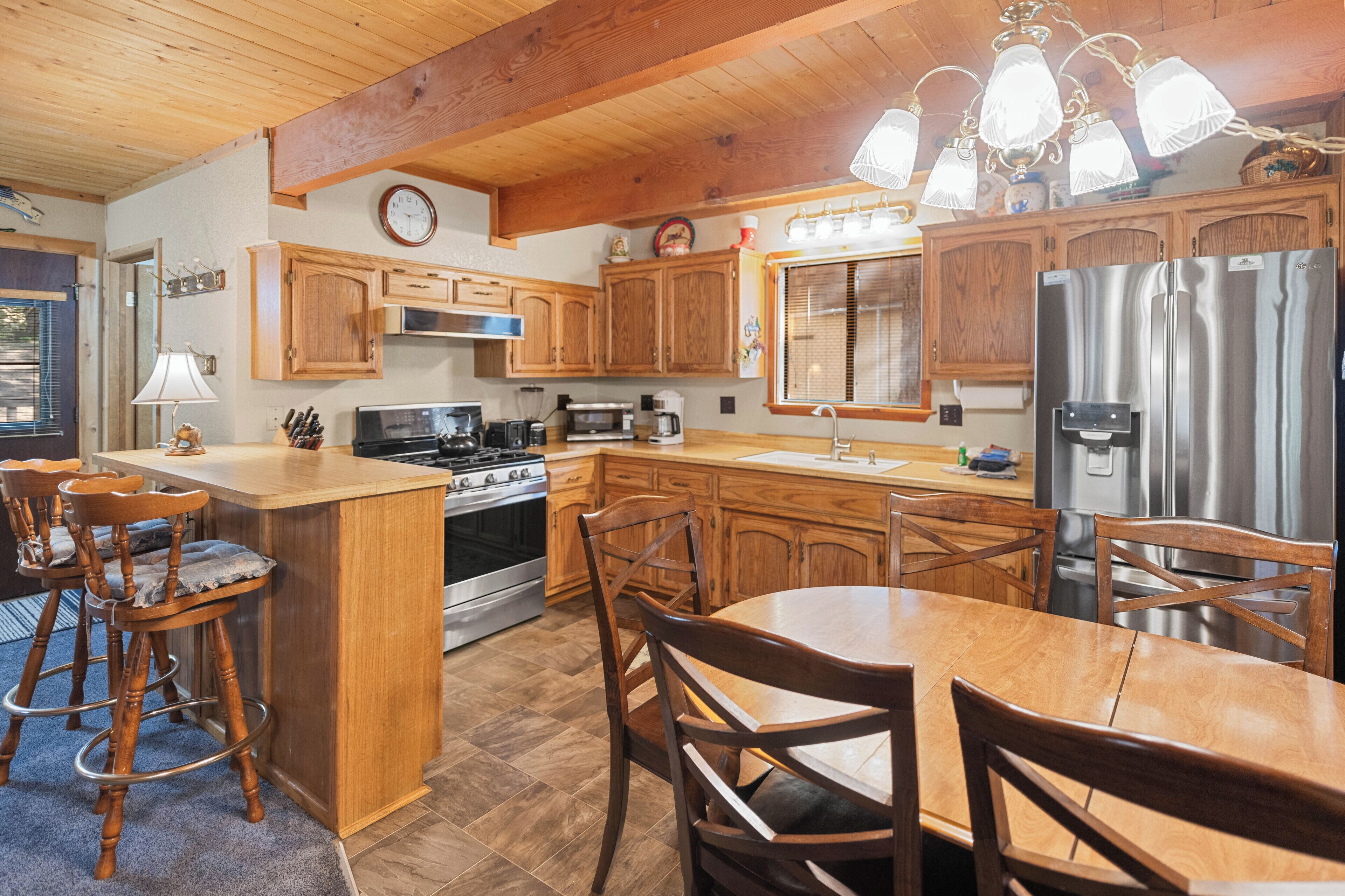 A kitchen with wooden cabinets, a stainless steel refrigerator, a stove, and a dining area with wooden chairs and a table.