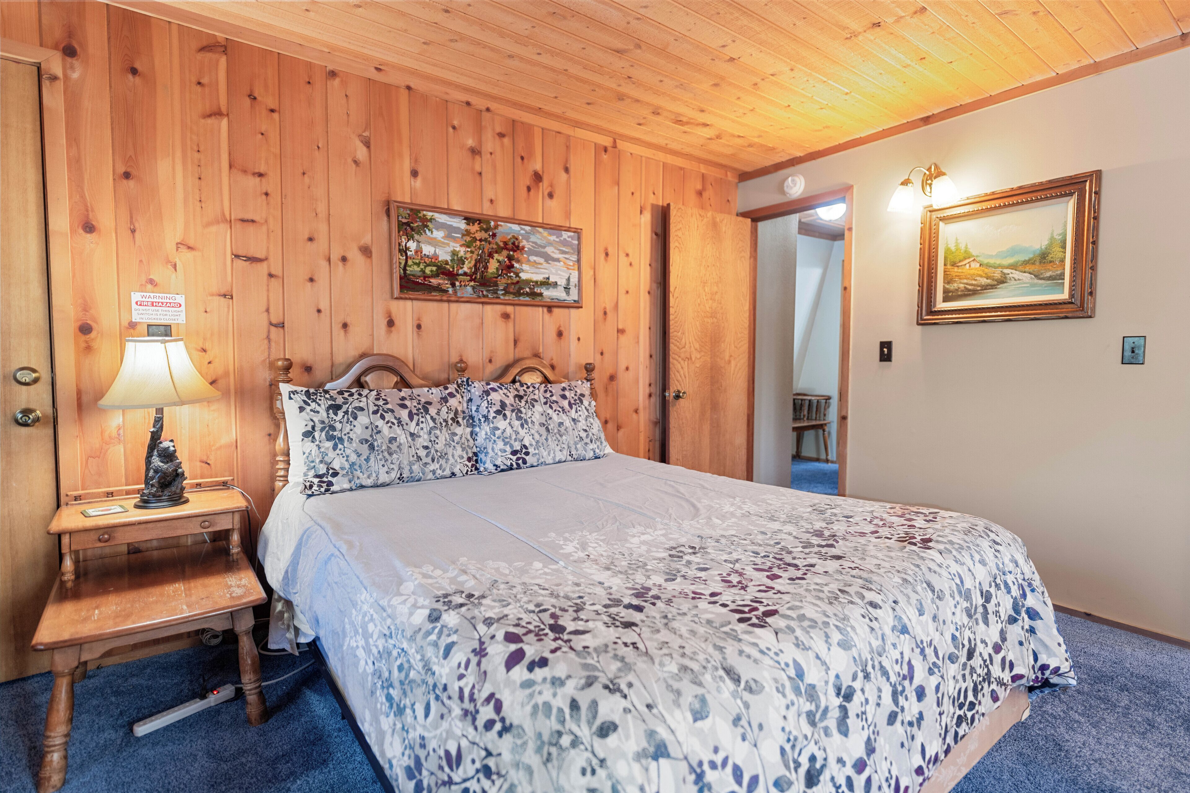 A wooden-paneled room with a bed, a nightstand, a lamp, and a painting on the wall.